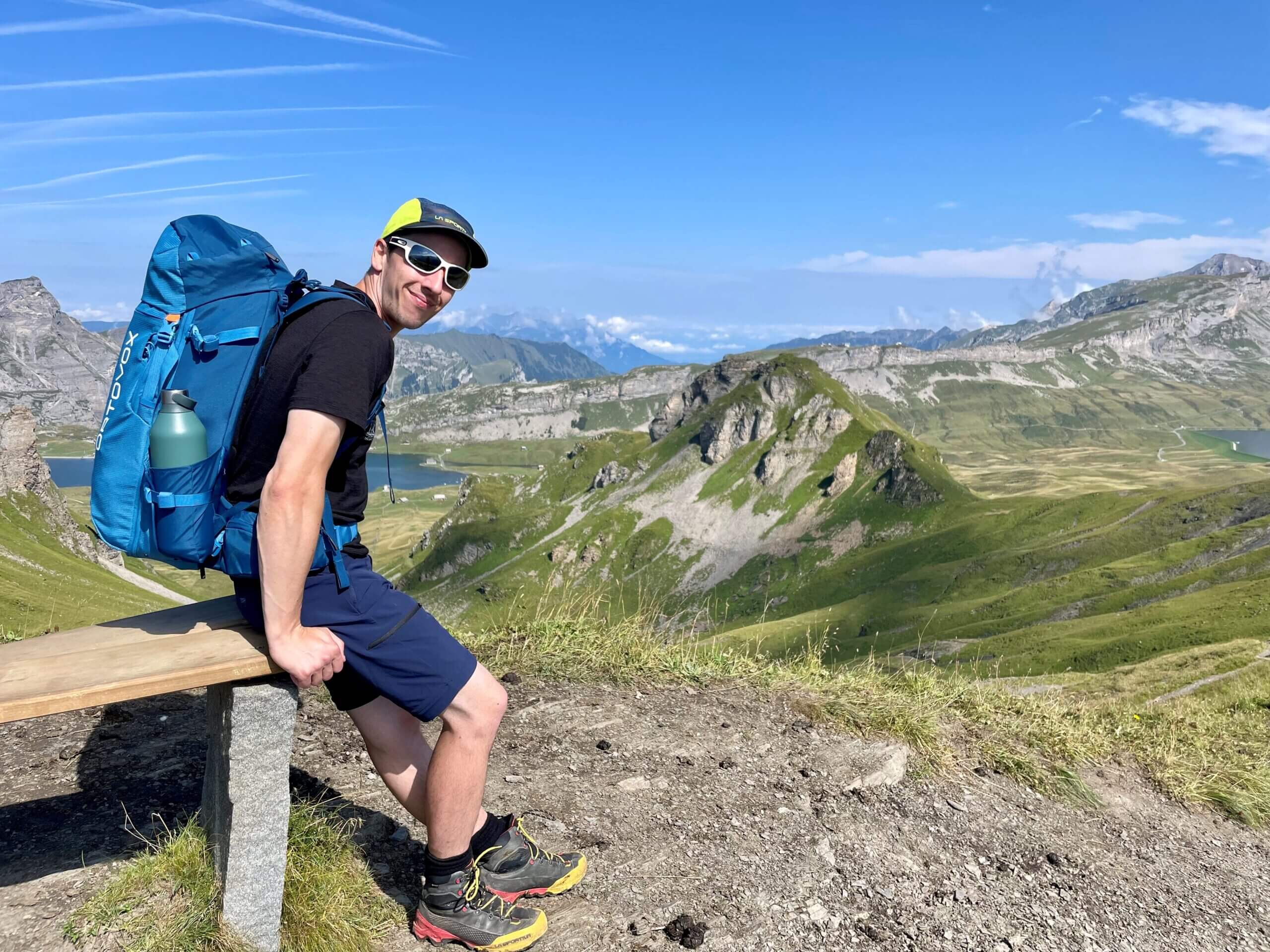 Wanderer mit Rucksack auf Bank in alpiner Landschaft während einer geführten Wandertour in der Schweiz.