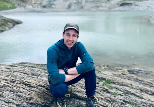 Person in Wanderkleidung posiert vor einem Bergsee in den Alpen.